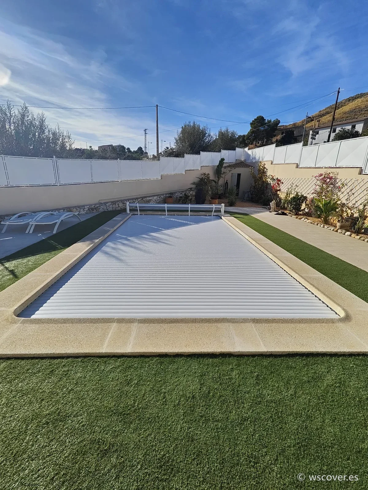 Cubierta de lamas automáticas blancas cerrada sobre piscina rectangular con césped