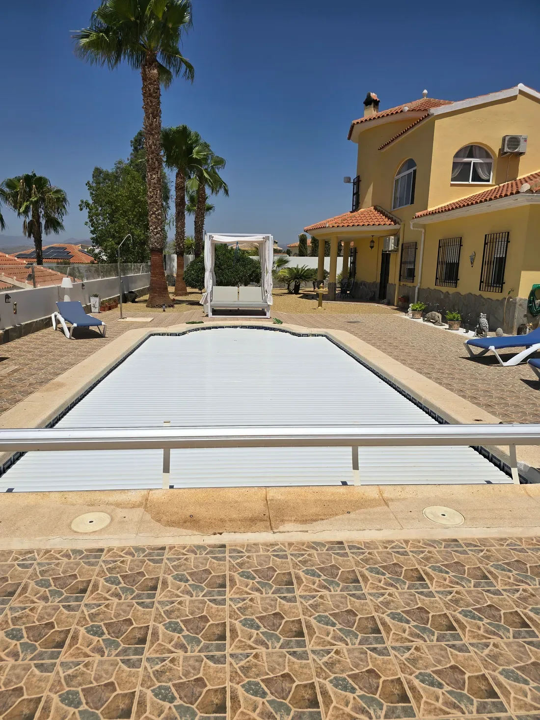 Cubierta de lamas automáticas cerrada sobre piscina rectangular en una villa con palmeras