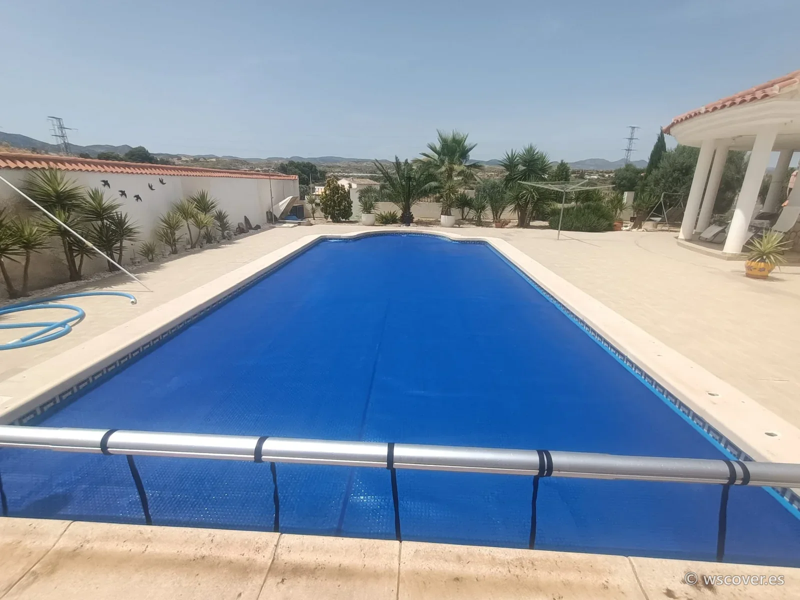 Cubierta de burbuja de 500 micras azul sobre piscina rectangular, con enrollador