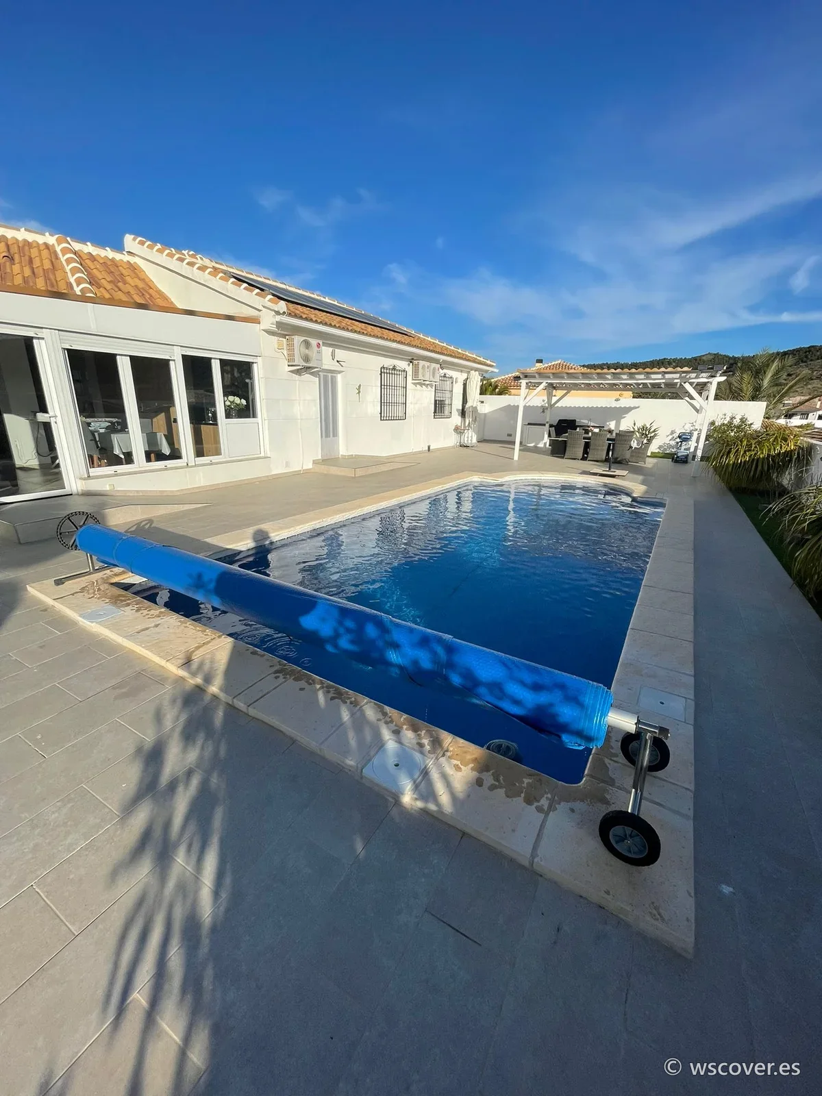 Cubierta de burbuja azul en su enrollador, junto a la piscina